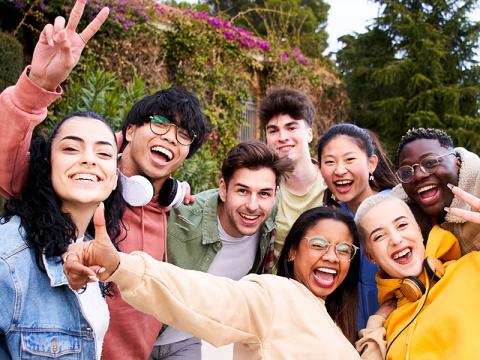 A racially diverse group of happy young adults pose for a group selfie