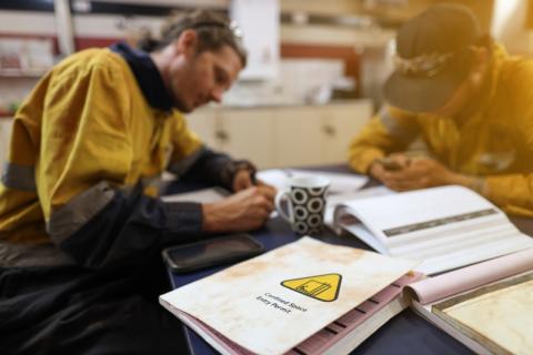 a worker in an industrial setting fills out paperwork at a desk with a binder and manual spread out around them